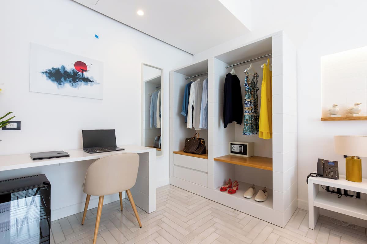 Ein modernes Zimmer mit Schreibtisch, Laptop, Stuhl und einem begehbaren Kleiderschrank mit Kleidung und Schuhen.