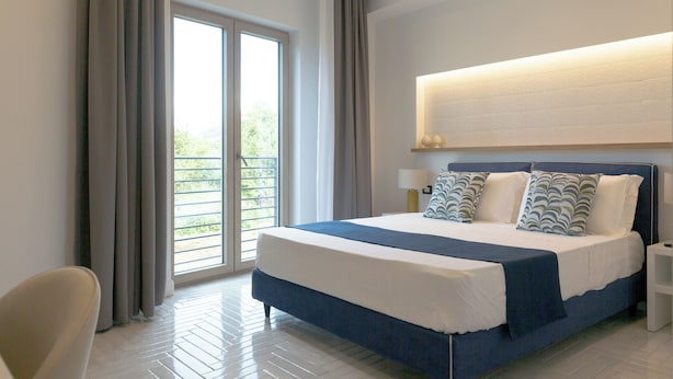 Ein modernes Hotelzimmer mit einem großen Bett, einem Nachttisch, einem Sessel und Blick auf einen Balkon.