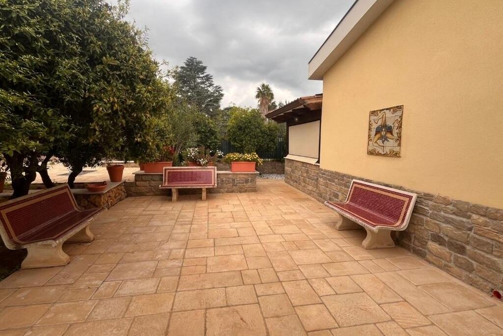 An outdoor patio with stone flooring, two red and white benches, and potted plants.