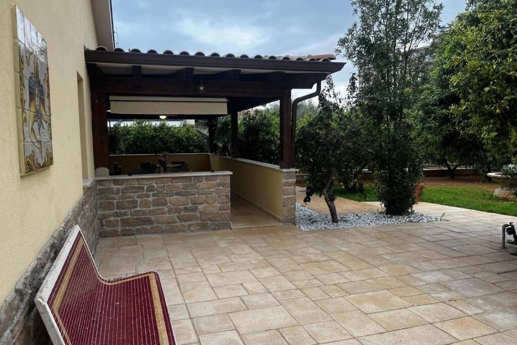 Un espace extérieur aménagé en terrasse, avec un banc en pierre, une pergola et un mur en pierre.