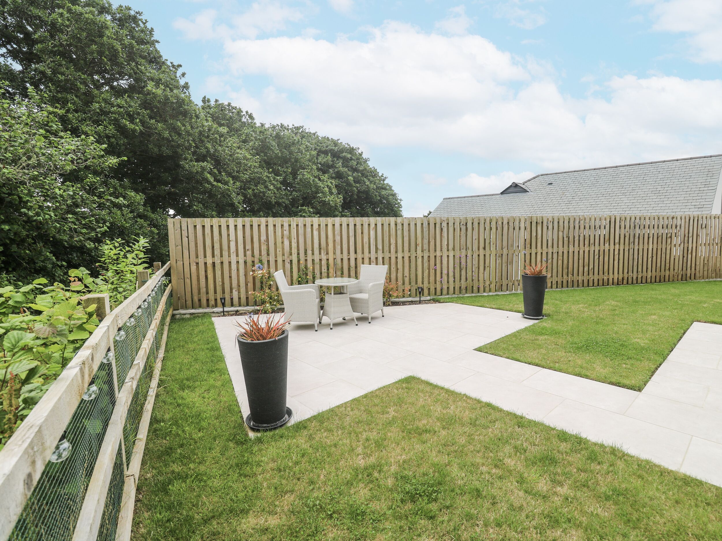 A patio area with a wooden fence, a small table with chairs, and potted plants.