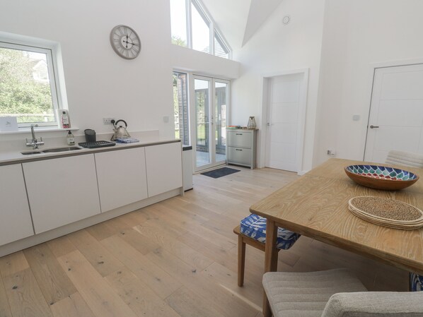 A modern kitchen with white cabinets, a wooden dining table, and a large window. - Kerrek Lodge (Falmouth)
