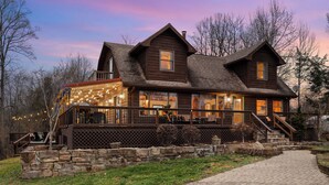 Een houten lodge met een veranda, stenen trappen en lichtjes.