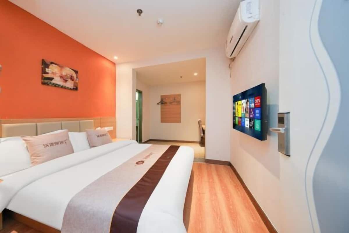 A hotel room with a bed, a wall-mounted TV, and a door leading to a bathroom.