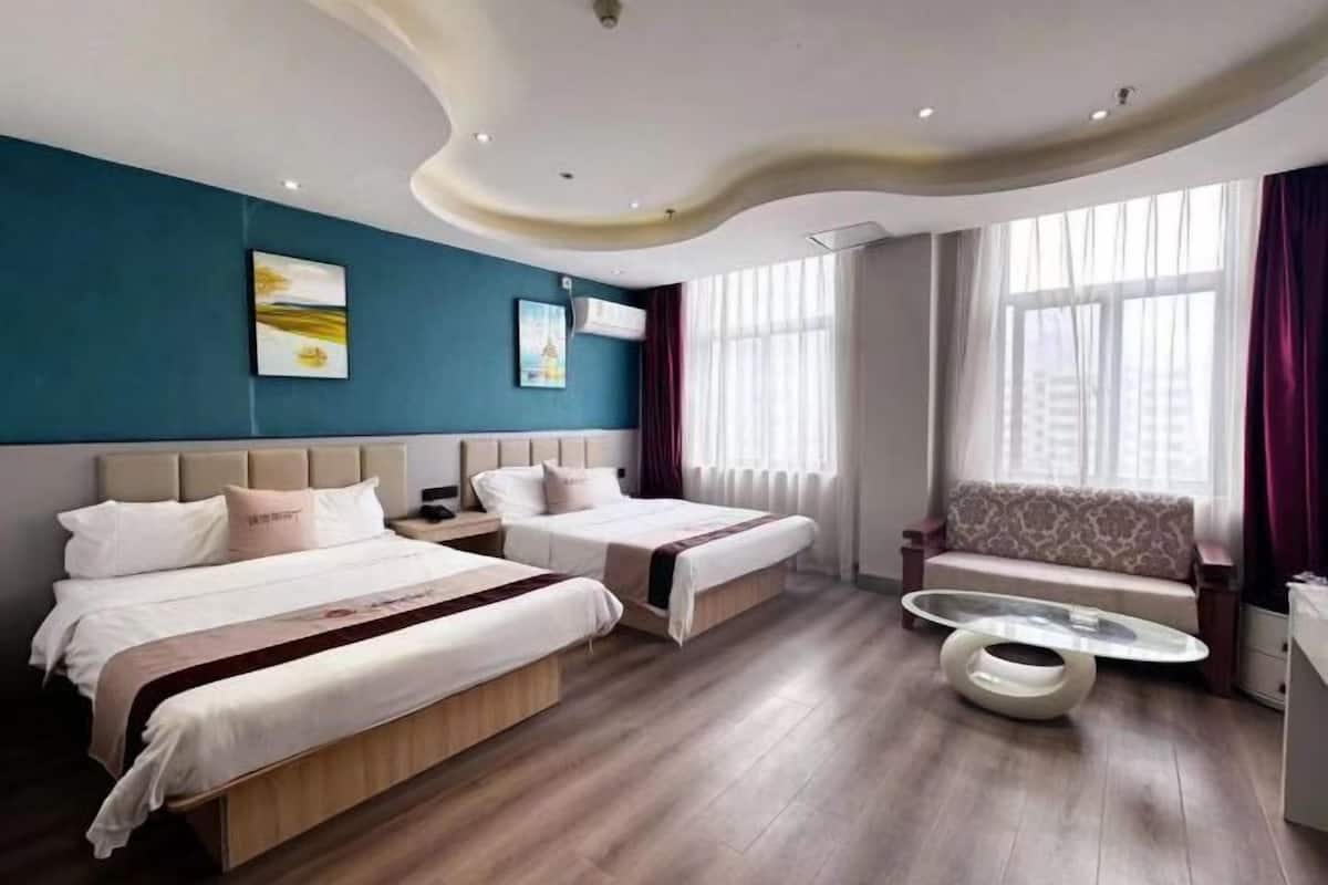 A hotel room with two beds, a sofa, a glass coffee table, and artwork on the walls.