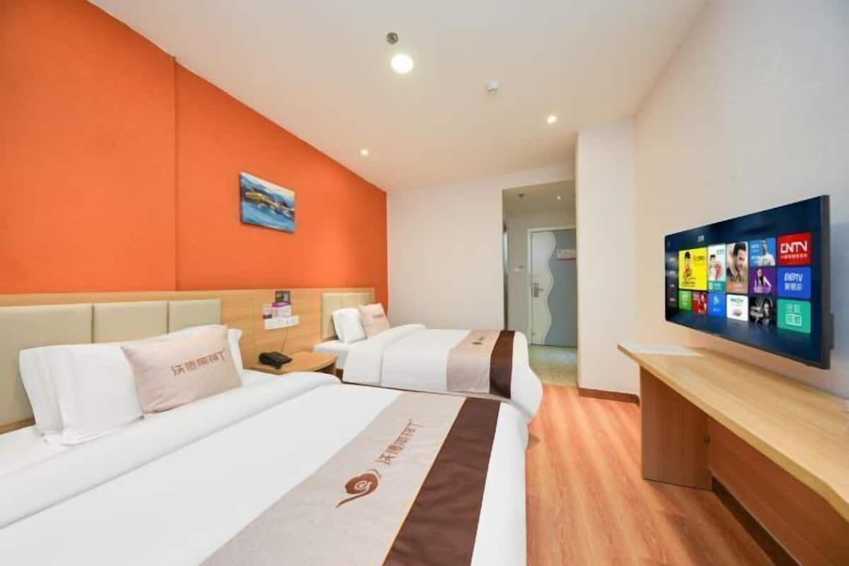 A hotel room with two beds, a TV, and a wooden desk.