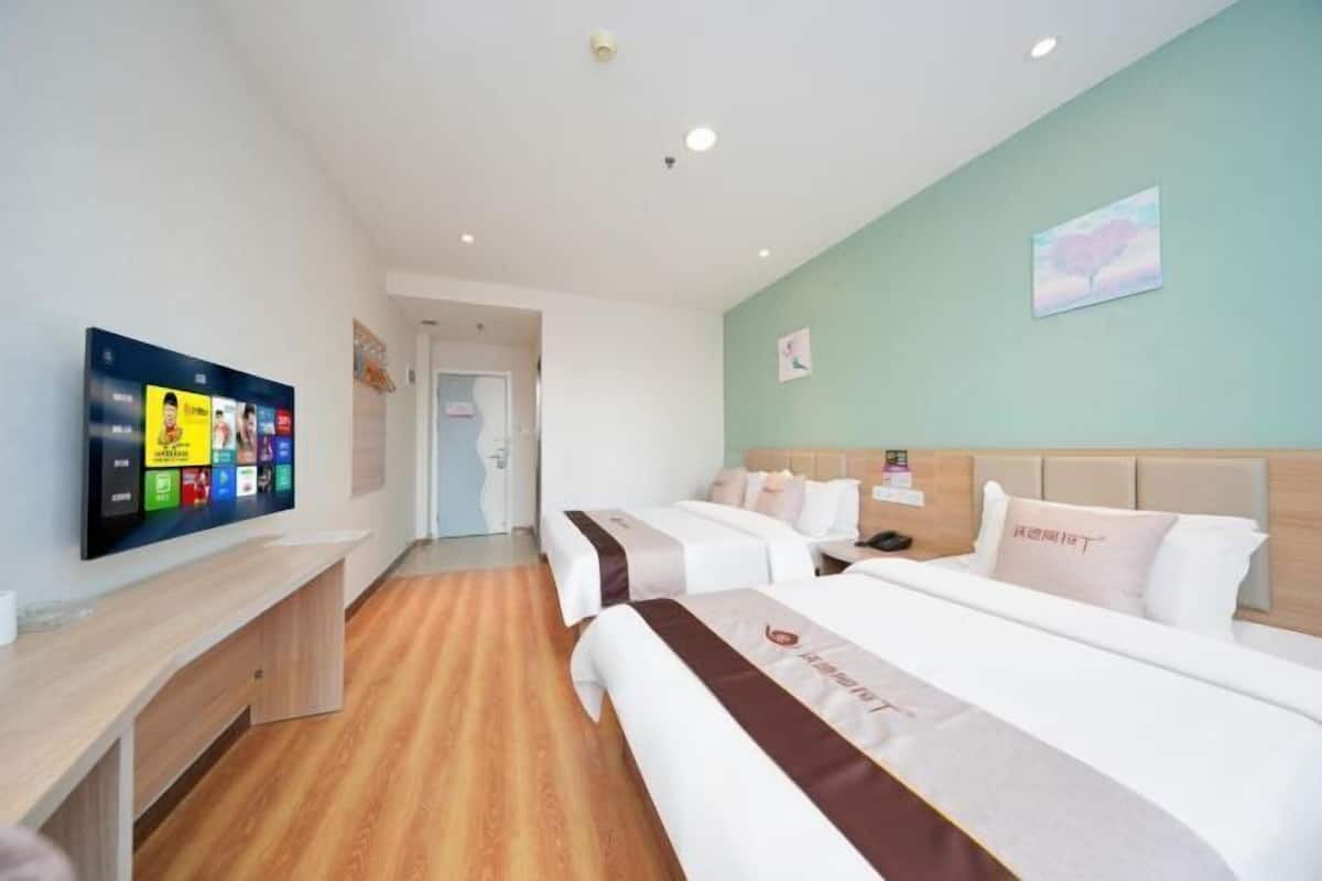 A hotel room with a bed, bedside table, and a wall-mounted TV displaying various channels.