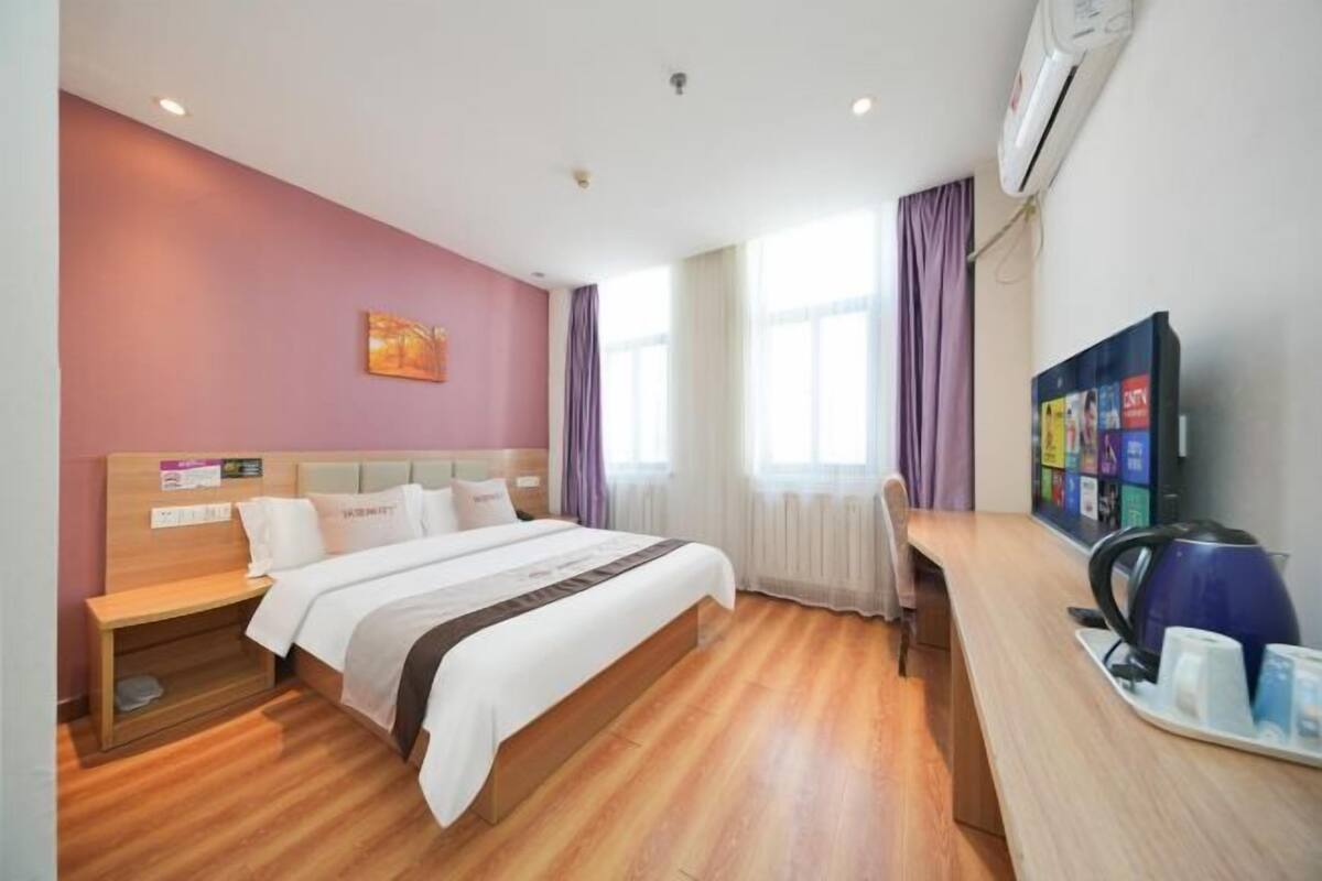 A hotel room with a bed, bedside table, desk, and a television.