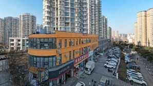 A high-rise building with a curved facade, a parking lot with multiple cars, and a clear sky. - Ward Aladdin Hotel (Changjiang East Road Huangdao Golden Beach Branch) (Qingdao)