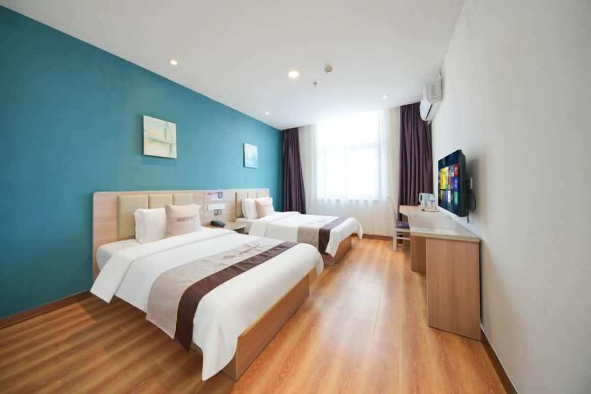 A hotel room with two beds, a desk, a TV, and a window with curtains.