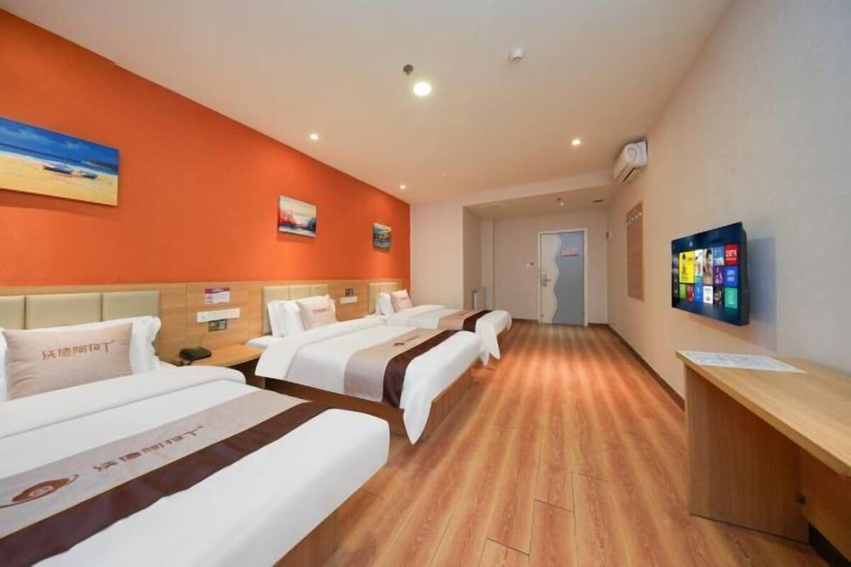A hotel room with three beds, a wooden floor, a TV, and a desk.