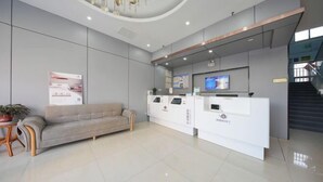 A modern reception area with a sofa, a reception desk, and a staircase. - Ward Aladdin Hotel (Changjiang East Road Huangdao Golden Beach Branch) (Qingdao)