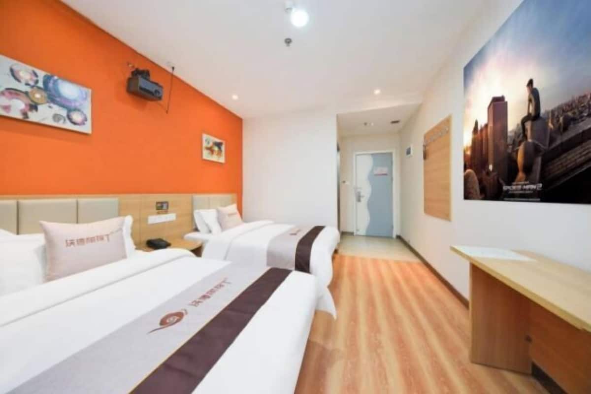 A hotel room with two beds, a desk, and a poster on the wall.
