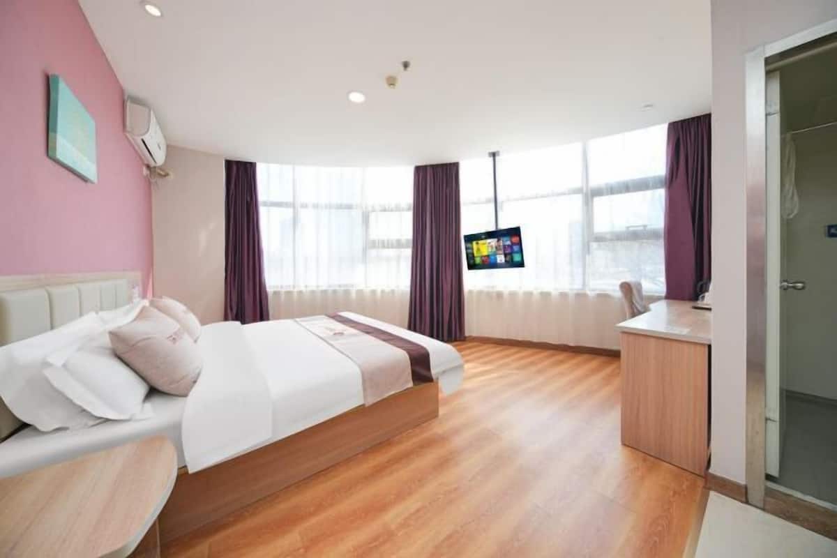 A modern hotel room with a bed, a desk, a TV, and a large window with curtains.