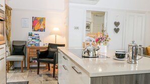 A modern kitchen with a central island, a dining area with chairs, a coffee maker, and decorative items. - The Bolt Hole (Kendal)