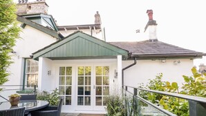 A patio with wicker furniture and a glass table, a white building with a green roof, and a white door with glass panels. - The Bolt Hole (Kendal)