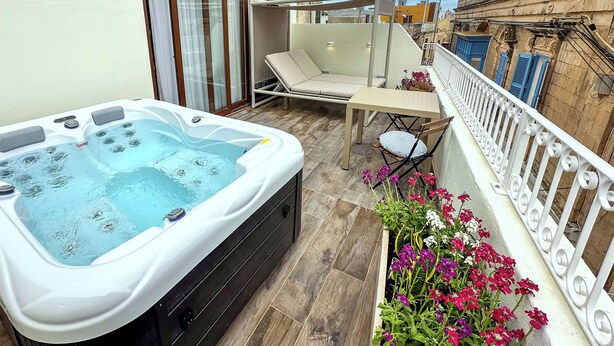 A balcony with a hot tub, a lounge chair, a table, and a flower planter. - Il Bekka Suites (Rabat)