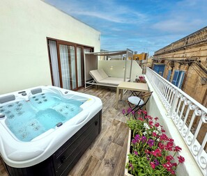 Un balcón con un jacuzzi, una silla de descanso, una mesa y una maceta con flores.