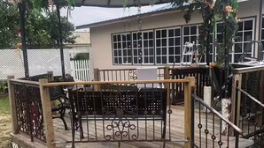 A gazebo with a wooden bench and metal railing, surrounded by a white fence and a house with large windows.