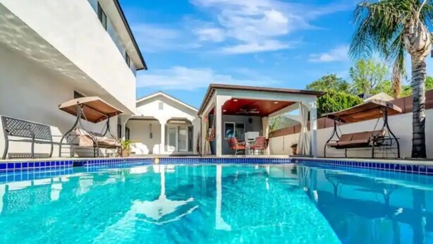 A swimming pool with a clear blue water, surrounded by a white building and a covered patio area with chairs and umbrellas. - Private 1-Bedroom Retreat with Poolside Vibes (Los Angeles)