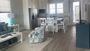 A modern kitchen with white cabinets, a stainless steel refrigerator, a microwave, and a dining area with white chairs and a table. - Posh, New, Ocean View Townhome in gorgeous Emerald Isle Perfect for families (Emerald Isle)