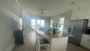 A modern kitchen with a central island, white cabinetry, and a view to the outside. - Posh, New, Ocean View Townhome in gorgeous Emerald Isle Perfect for families (Emerald Isle)