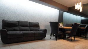 Un salon moderne avec un canapé gris foncé, une table à manger avec des chaises et une grande fenêtre laissant entrer la lumière naturelle.
