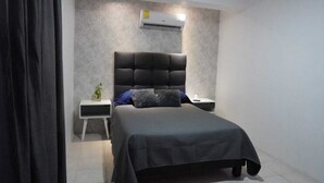 Une chambre à coucher avec un lit, une table de chevet, un climatiseur fixé au mur et une petite plante.