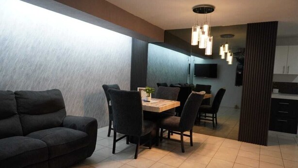 Un espace repas moderne avec une table et des chaises en bois, un canapé et un téléviseur fixé au mur.