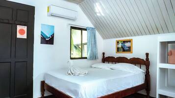 A bedroom with a wooden bed, white bedding, a window with a view, an air conditioner, and a door.