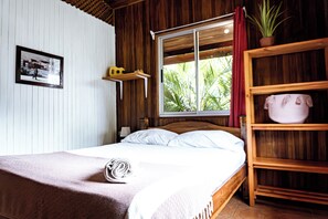 A wooden-framed bed with white linens, a rolled towel, and a shelf with a potted plant. - Surf Paradise (Cobano)