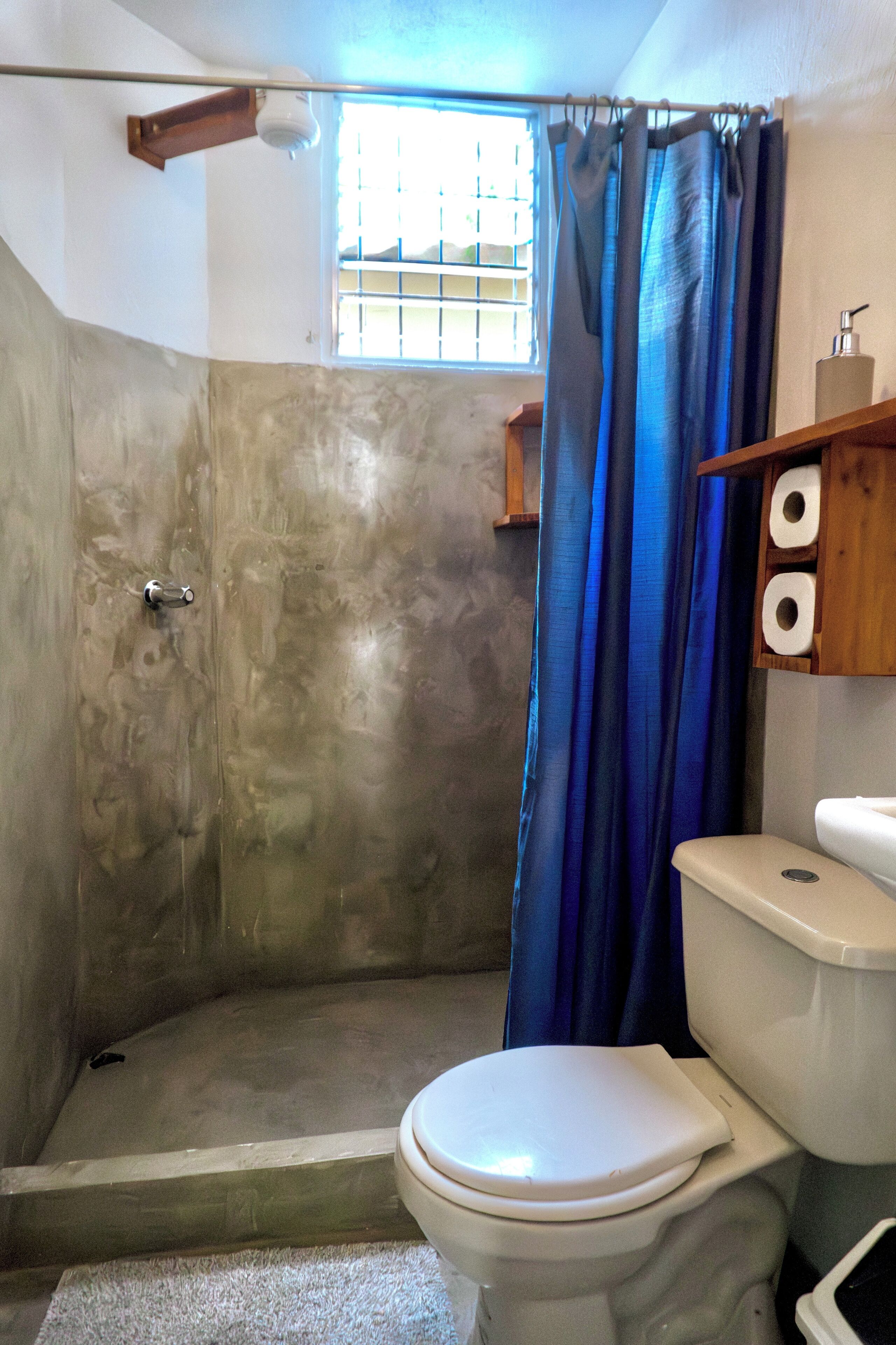 A bathroom with a shower, toilet, and a window with bars.