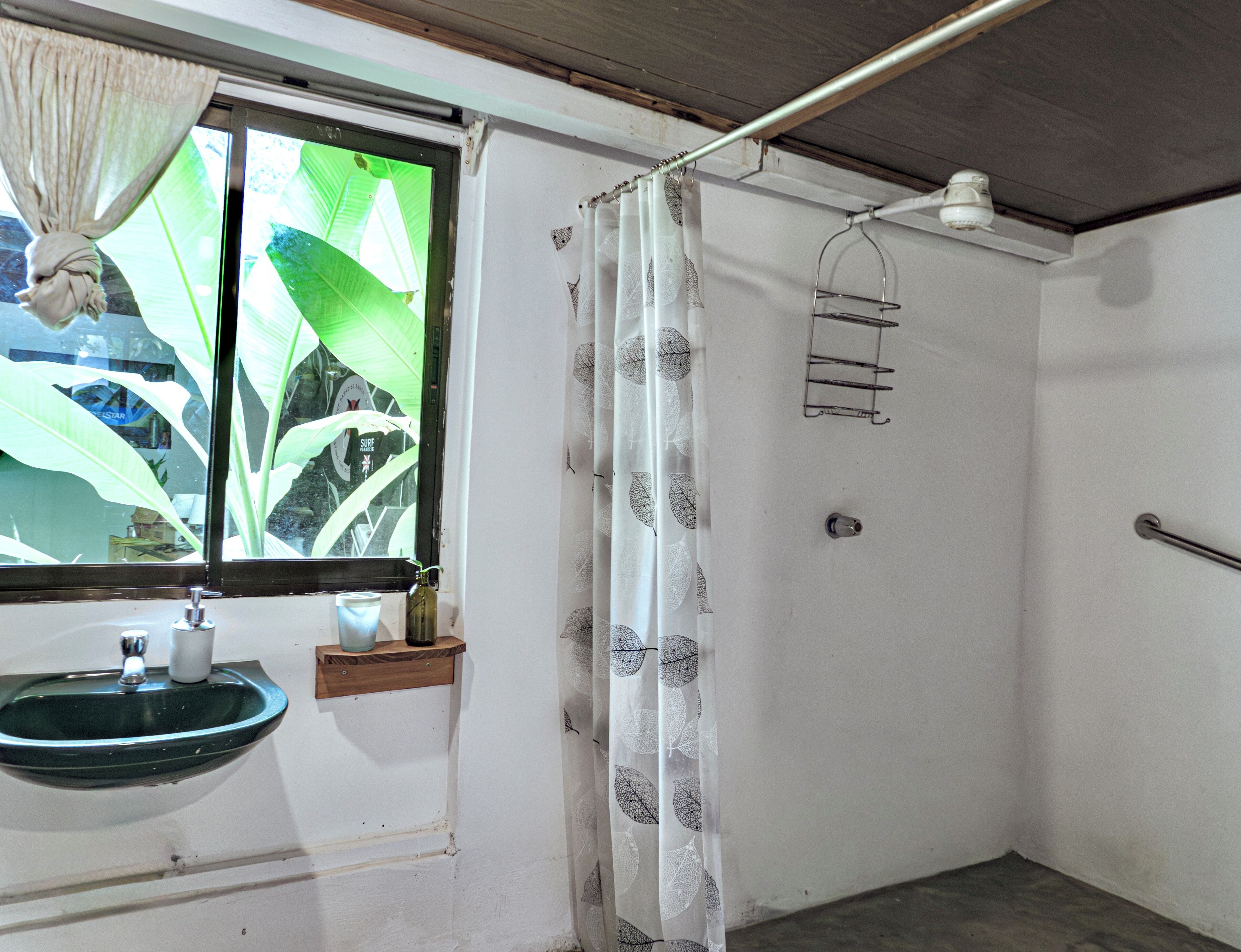Un baño con ventana, lavamanos, cortina de ducha y un perchero para toallas.