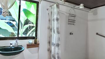 Un baño con ventana, lavamanos, cortina de ducha y un perchero para toallas.