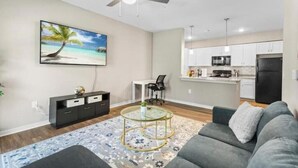 Een moderne woonkamer met een grijze bank, een glazen salontafel en een schilderij van een strandgezicht.