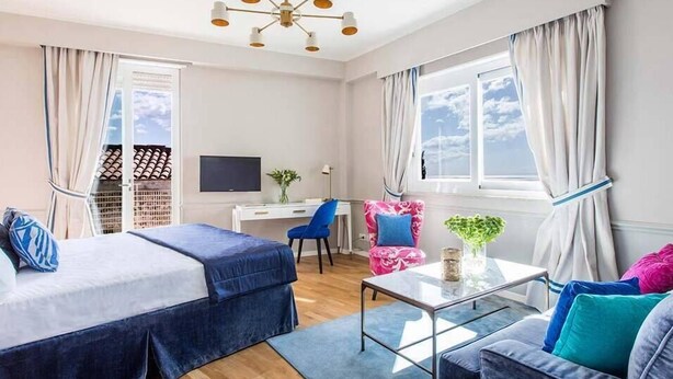 Een hotelkamer met twee bedden, een bureau, een stoel, een bank, een televisie en een raam met gordijnen.