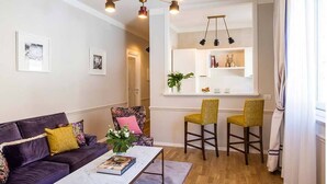 Un salon avec un canapé violet, deux fauteuils, une table basse et un lustre moderne.