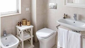 A modern bathroom with a bidet, toilet, sink, and a window.