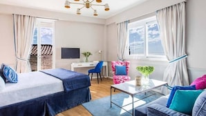A hotel room with two beds, a desk, a chair, a sofa, a TV, and a window with curtains.