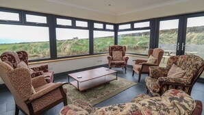 A spacious room with large windows, a wooden coffee table, and floral-patterned sofas. - Castell Y Garn (Newport)