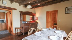 A dining room with a long table set for four, wooden chairs, a wooden cabinet with a mirror, and a clock on the wall. - Castell Y Garn (Newport)