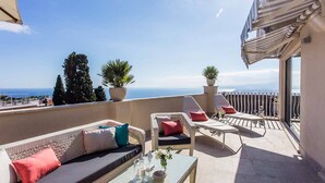 A terrace with wicker furniture, a glass table, and potted plants.