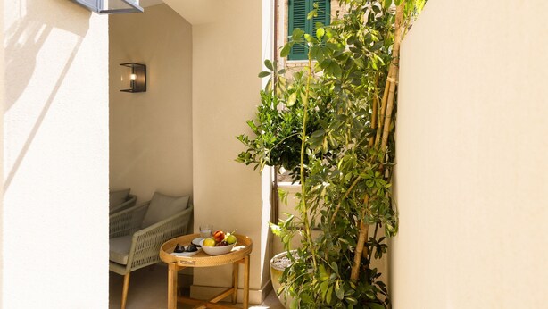 A narrow outdoor space with a wicker table, a bowl of fruit, and a potted plant. - Green Palm (Taormina)