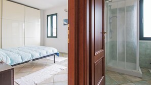 Un dormitorio con cama, armario de madera, cabina de ducha y ventana.