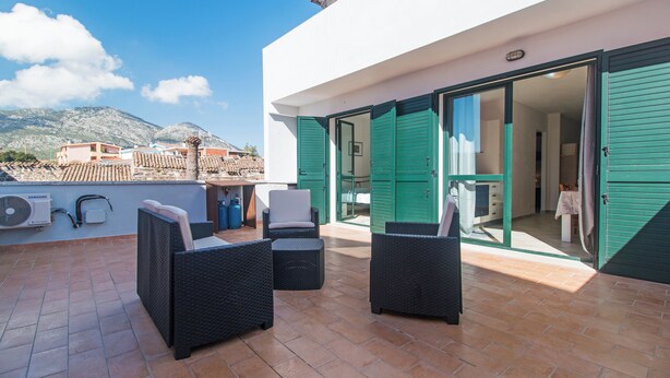 Un patio al aire libre con mobiliario de mimbre, un acondicionador de aire Samsung y vistas a la ciudad y montañas.