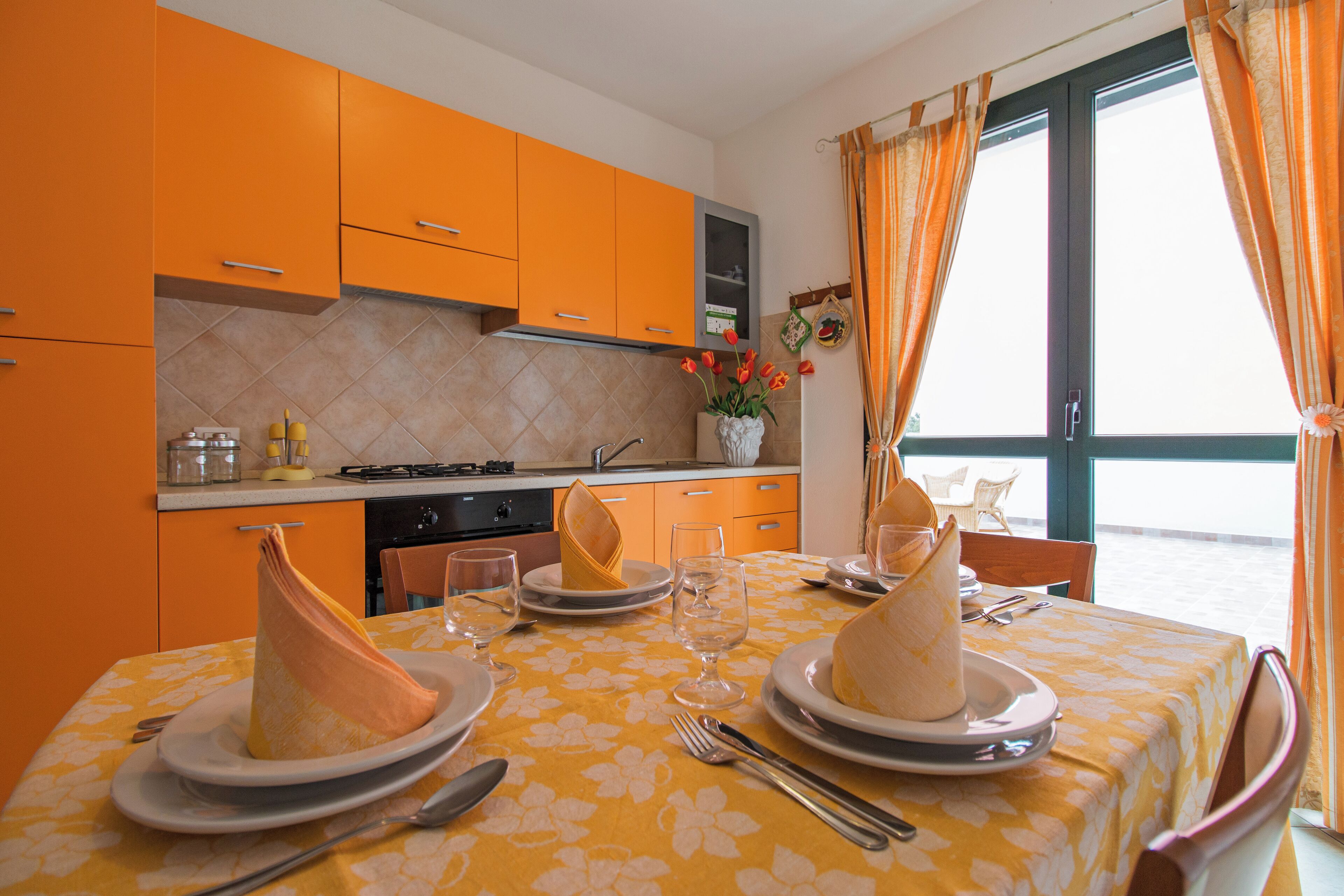 A dining area with a table set for two, featuring plates, cutlery, and a vase with flowers.