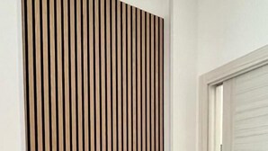 Un couloir avec un mur recouvert de panneaux de bois verticaux et une porte blanche fermée.