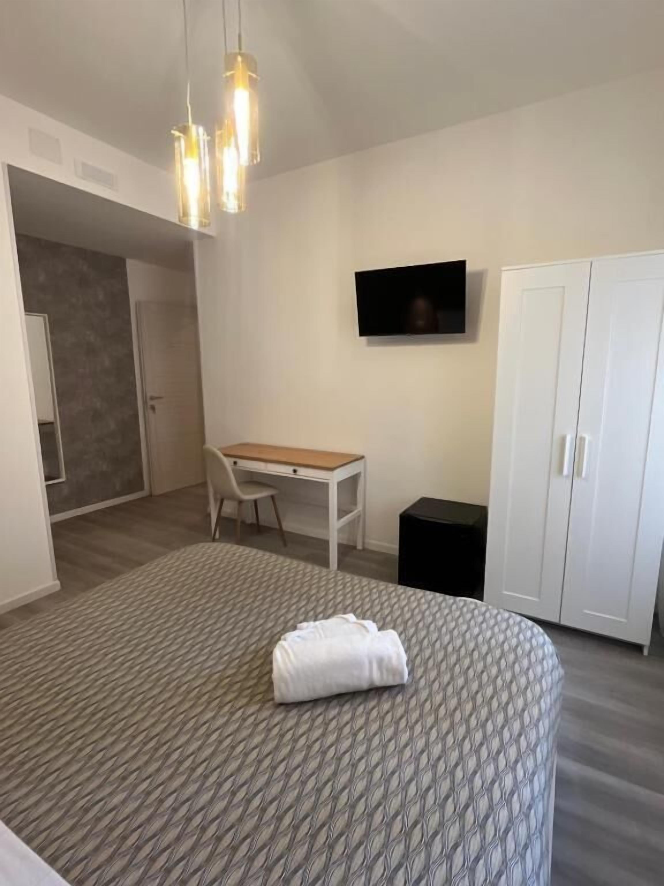 A modern bedroom with a bed, a desk, a TV, and a wardrobe.