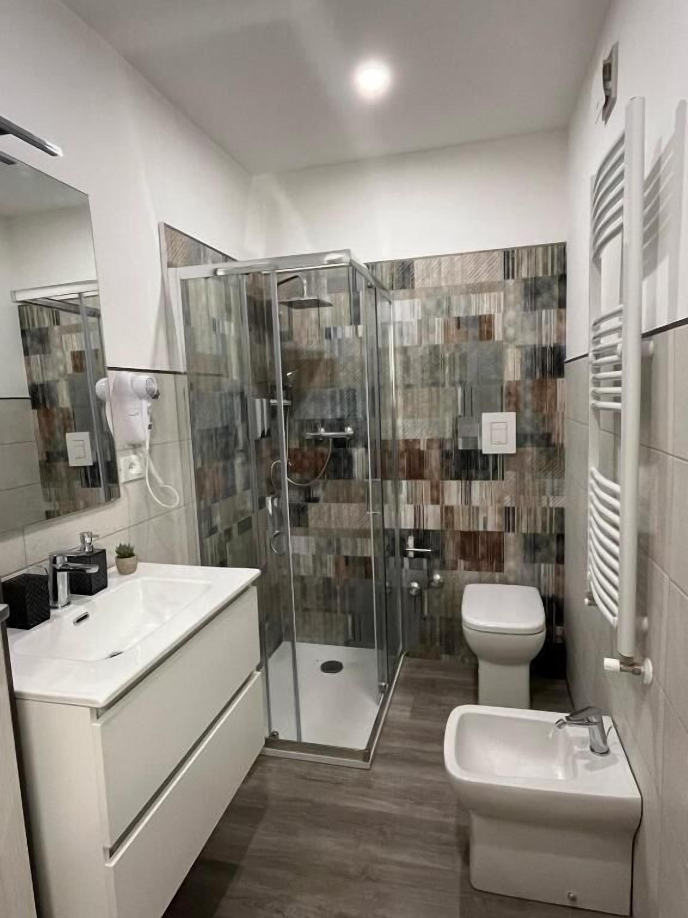 Ein modernes Badezimmer mit einer gläsernen Duschkabine, einem weißen Waschbecken und einer Toilette.
