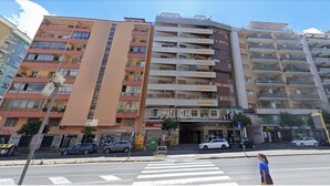 Un immeuble résidentiel à plusieurs étages, doté de balcons, d’un passage piéton et de voitures garées.